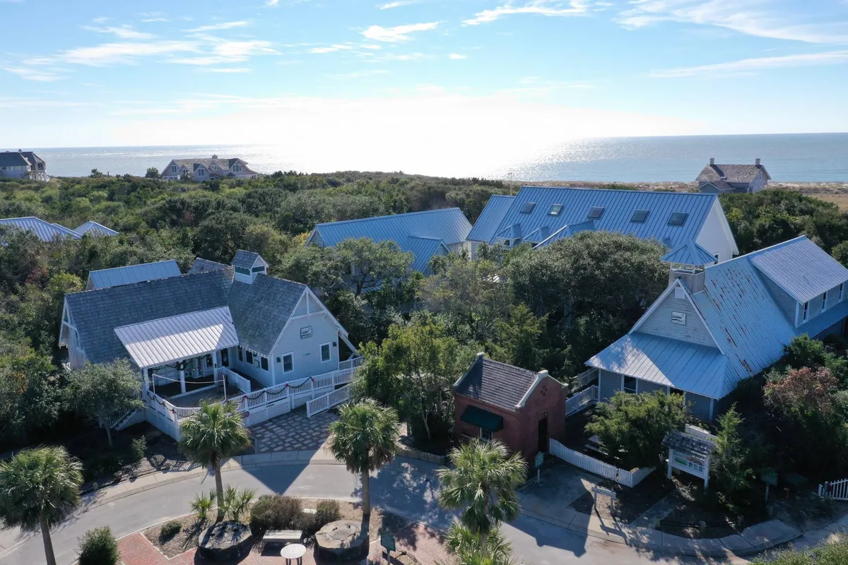 An inviting exterior view of a private home nestled amid lush greenery with unobstructed ocean views. The wraparound deck, outdoor seating, and pathway highlight the home's secluded nature and seamless connection to the outdoors. The tranquil setting is ideal for relaxation, morning coffee, or stargazing by the sea.
