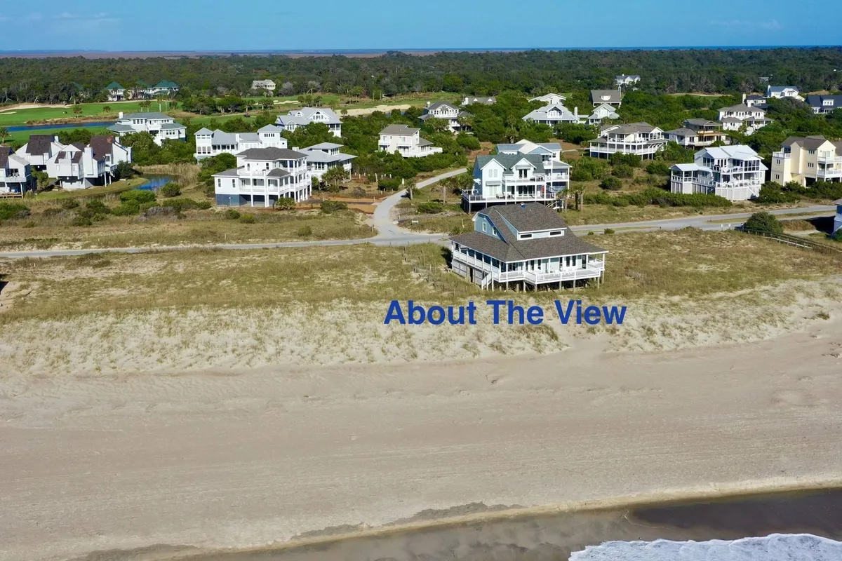 A beachfront property with direct access to the sand and ocean waves. The image shows the house nestled among other homes, with visible sand dunes and open sky. The space is set up for relaxed outdoor gatherings and family-friendly activities.