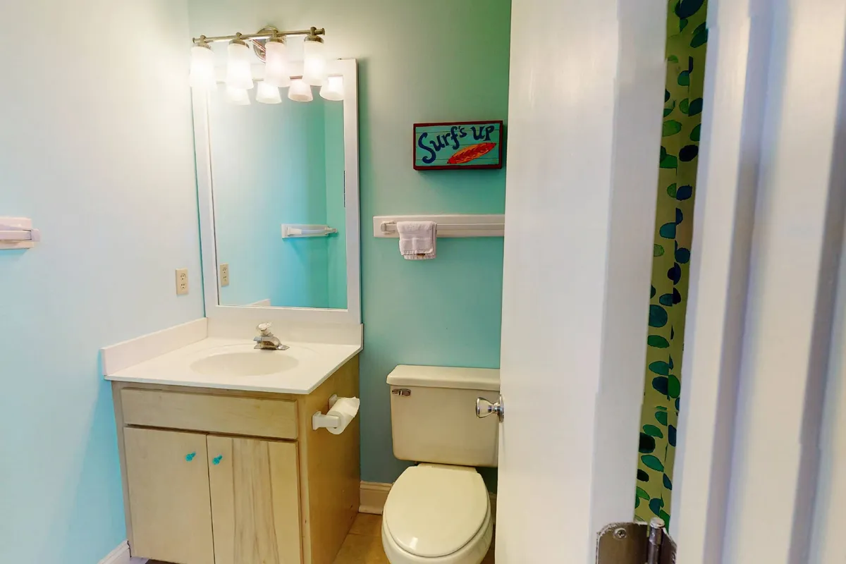 A cheerful bathroom with a vanity, colorful wall art, and a mirror, suggesting a refreshing spot to clean up after outdoor activities. The mood is playful and inviting, oriented toward post-beach routines.