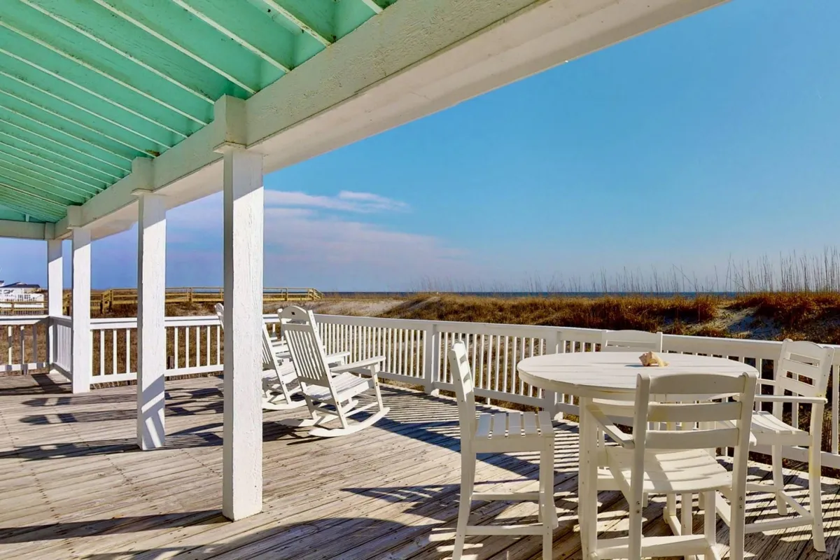 An inviting outdoor seating area on a wooden deck, offering a scenic view of the beach and ocean. The setting is ideal for family gatherings, morning coffee, or watching the sun rise and set. The arrangement suggests privacy and comfort, surrounded by the natural landscape.