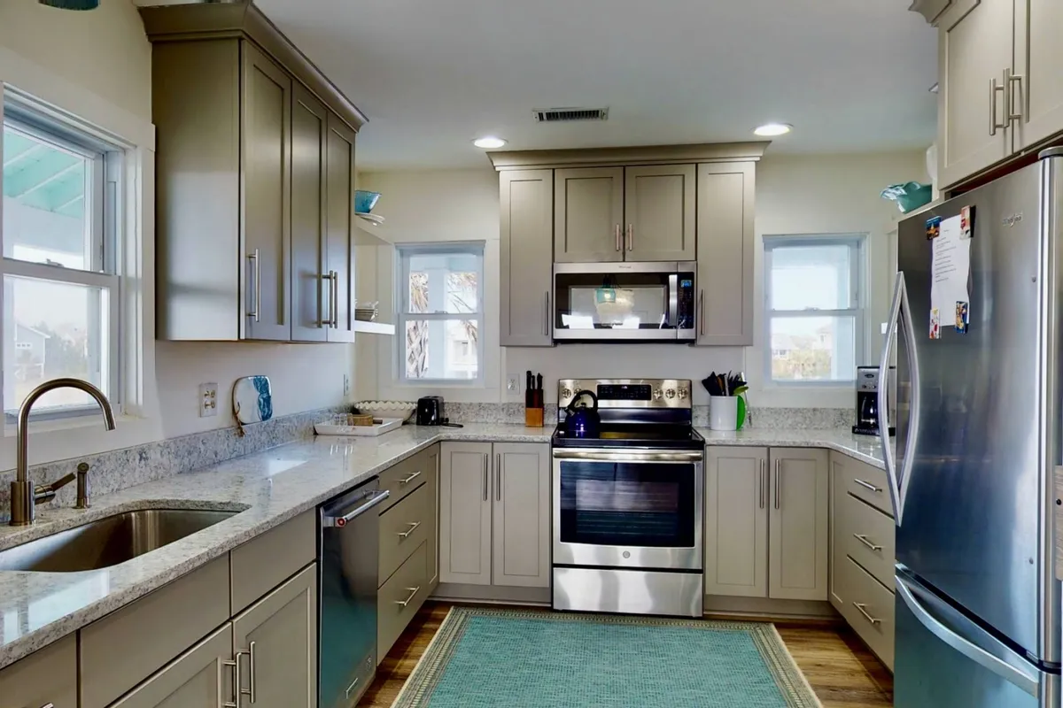 A bright, modern kitchen featuring stainless steel appliances, granite countertops, and a window that brings in natural light. The scene includes a spacious prep area ideal for cooking and gathering, with subtle decorative touches that enhance the welcoming feel.