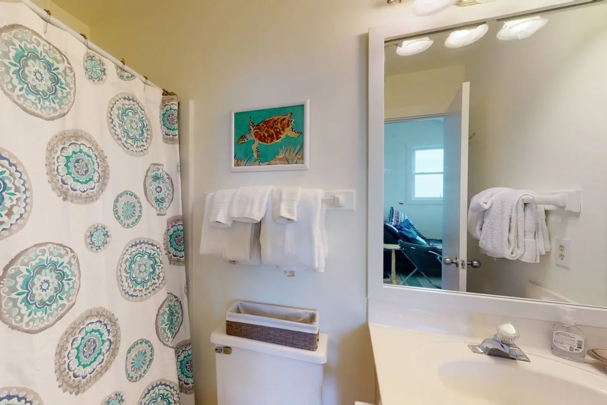 A modern bathroom with a clean sink area, fluffy towels, a colorful shower curtain, and framed artwork on the wall. The space feels fresh, calm, and inviting, with thoughtful touches that enhance comfort and convenience.